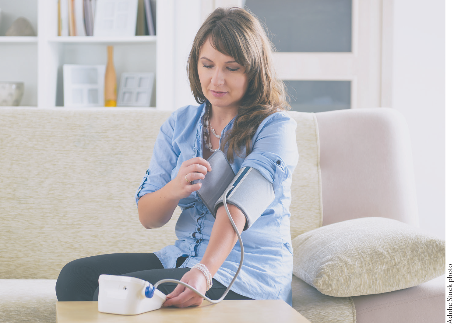A woman preparing to test her blood pressure in a living room.
