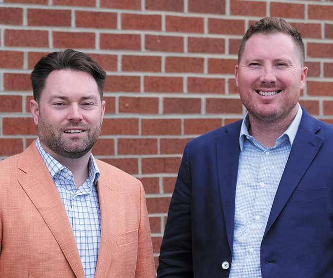 Secured Tech Solutions President and CEO Nate Holmes and Chief Revenue Officer Chris Hawkins standing in front of a brick wall