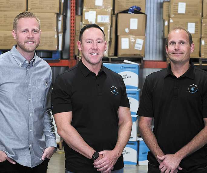 Screenbroidery Chief Operating Officer Gabe Peters, founder and CEO Thomas Rector and Chief Sales Officer Mark Myers standing in a warehouse