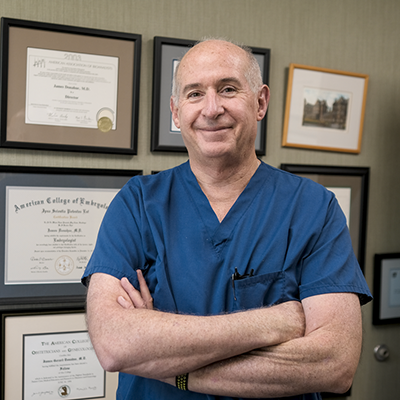 Dr. Jim Donahue wearing scrubs standing in front of a wall of degrees