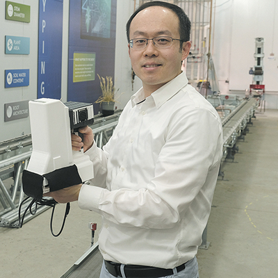 Purdue agricultural and biological engineering professor Jian Jin holding a handheld device farmers can use in the field for
                early detection of plant diseases.