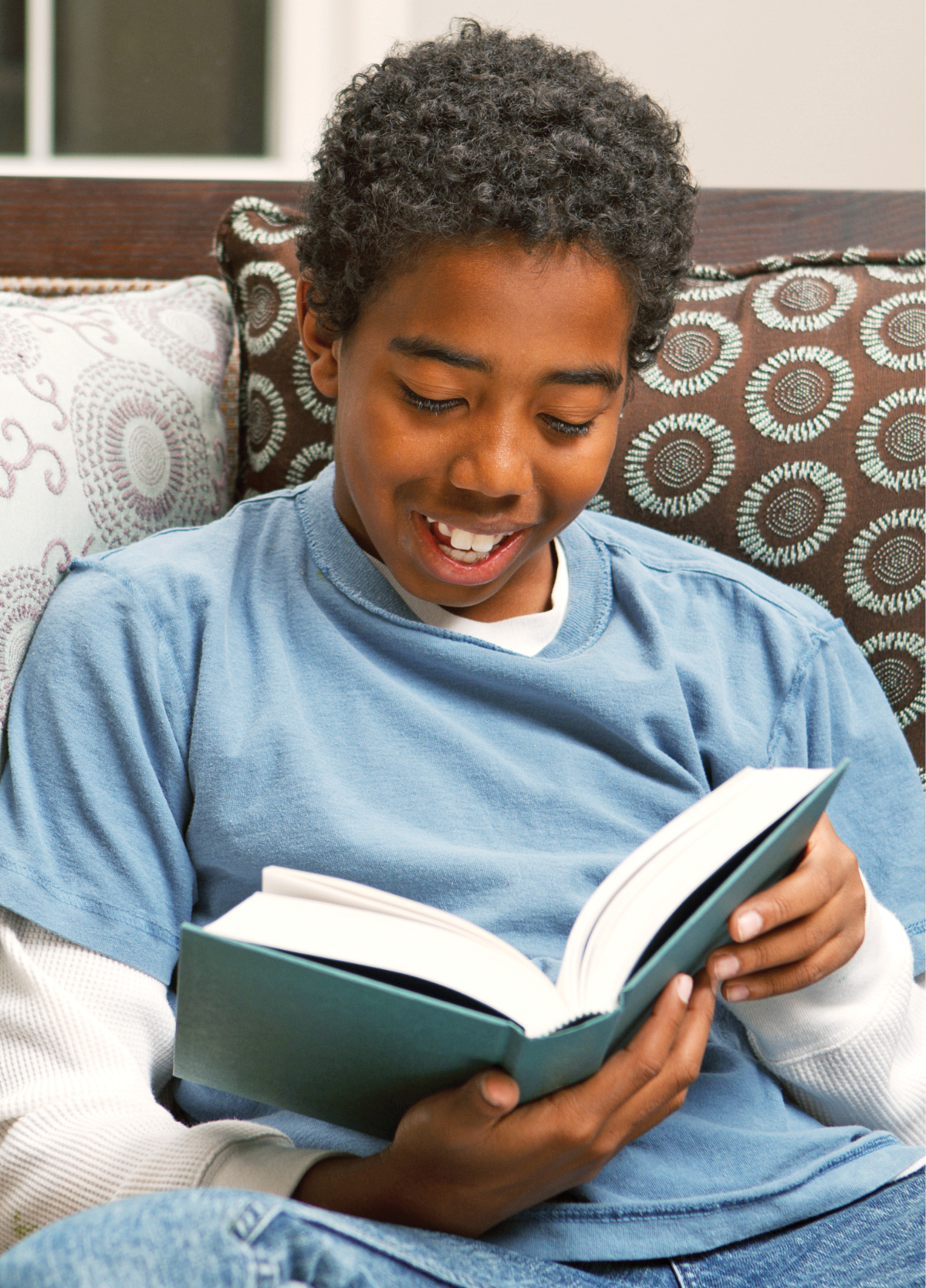  Photograph of a smiling child seated against pillows reading a hardcover book