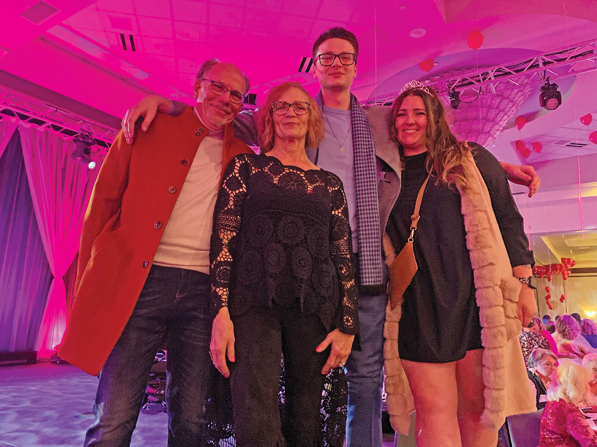 A photograph taken from a low angle pointing up of a family of four: Wife, husband, son, and daugher in pink light on an event stage