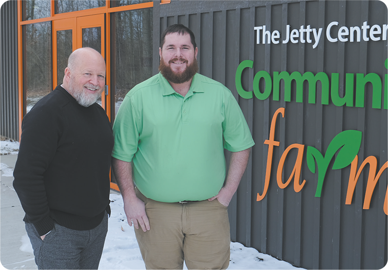 Tom Bannon and Mikkal Hodge stand in front of a building with signage reading The Jetty Center at Community Farm