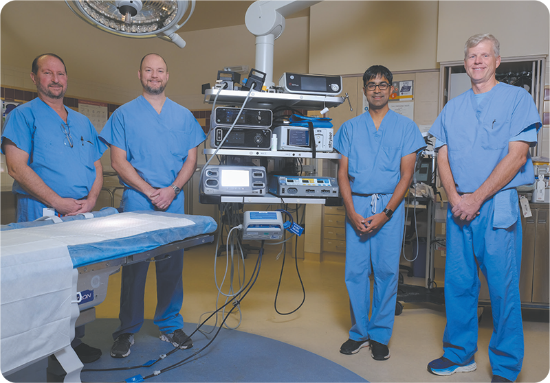 Group photograph of Dr. Jon Mandelbaum; Dr. James Raybourn; Dr. Dipen Maun and
            Dr. Wade Wrightson of Enhanced Recovery After Surgery, all wearing blue scrubs standing in an operating room