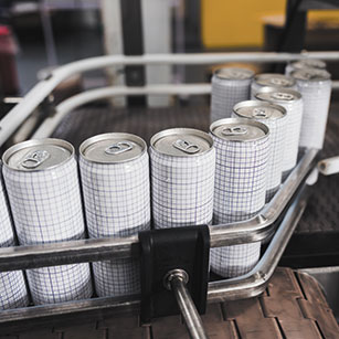 A line of tab-top cans with white labels covered in dark gray grids along the metal bars of an assembly line device