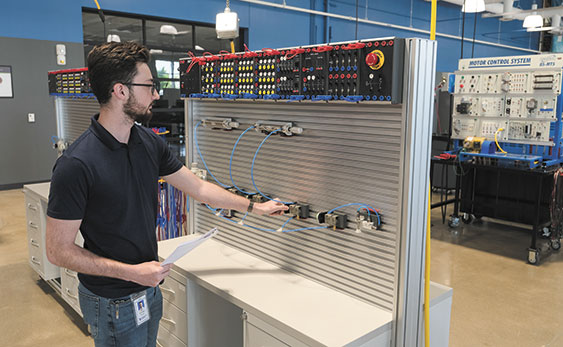 A bearded man with dark hair and glasses adjusting a lever on a vertical panel covered in wires and components