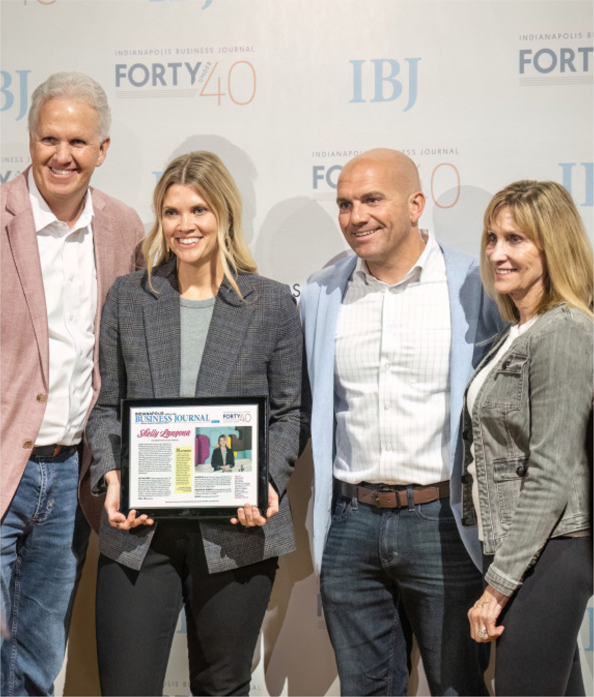 Four smiling attendees posed in front of an IBJ Media 40 under Forty branded backdrop