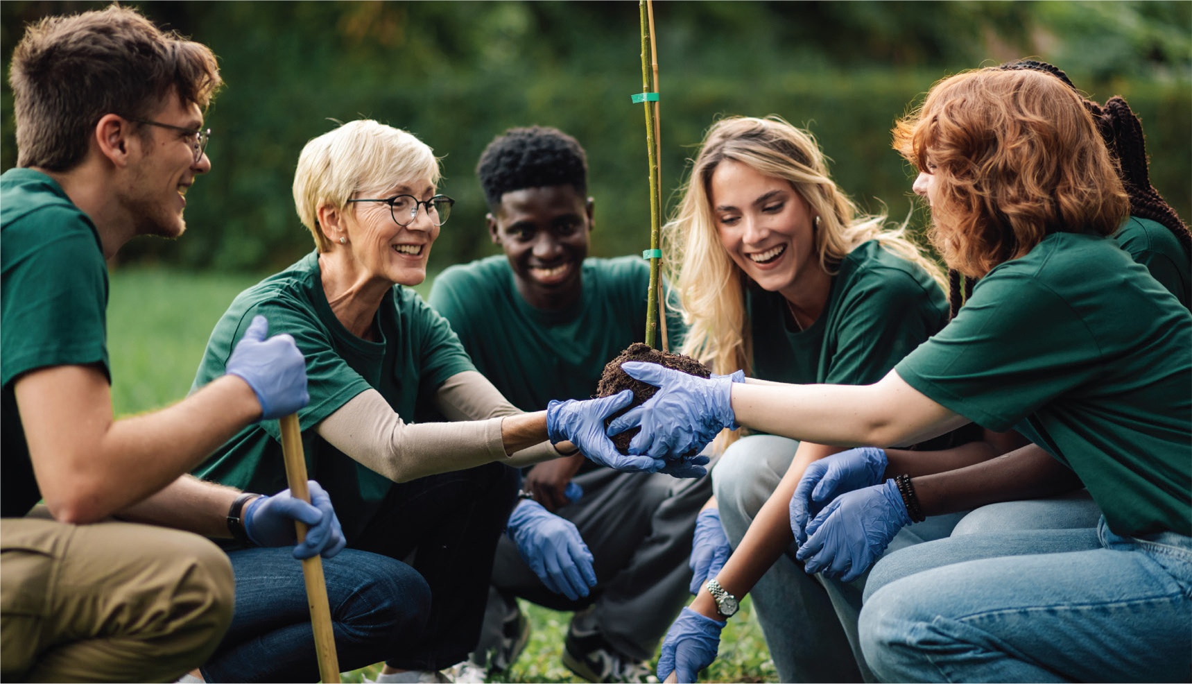 Six crouching volunteers smile around a clump of dirt held in the center by two of them