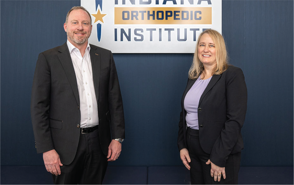 2 members of Indiana Orthopedic Institute posed in front of a sign for the organization