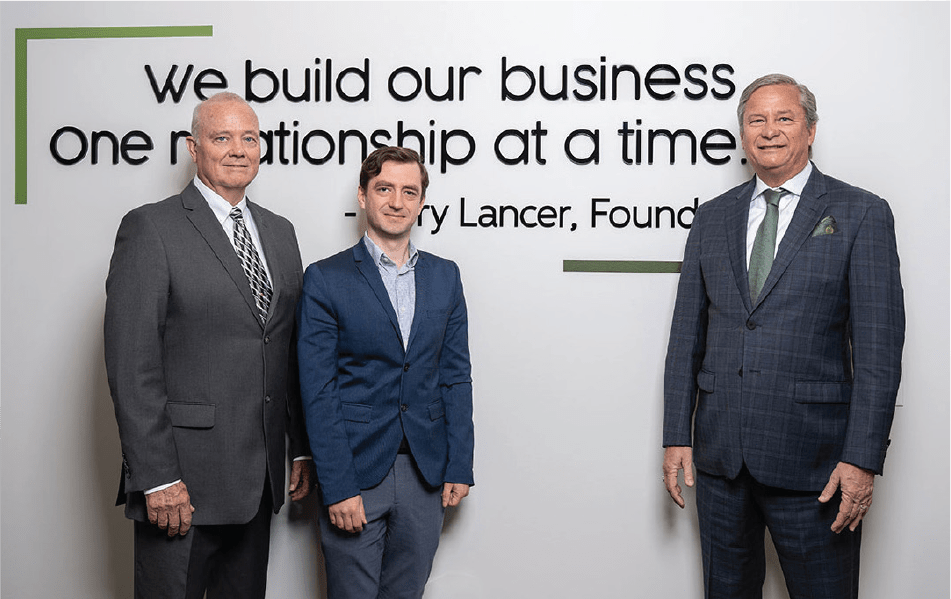 3 members of Lancer Associates posed in front of a wall mounted quote of their founder's