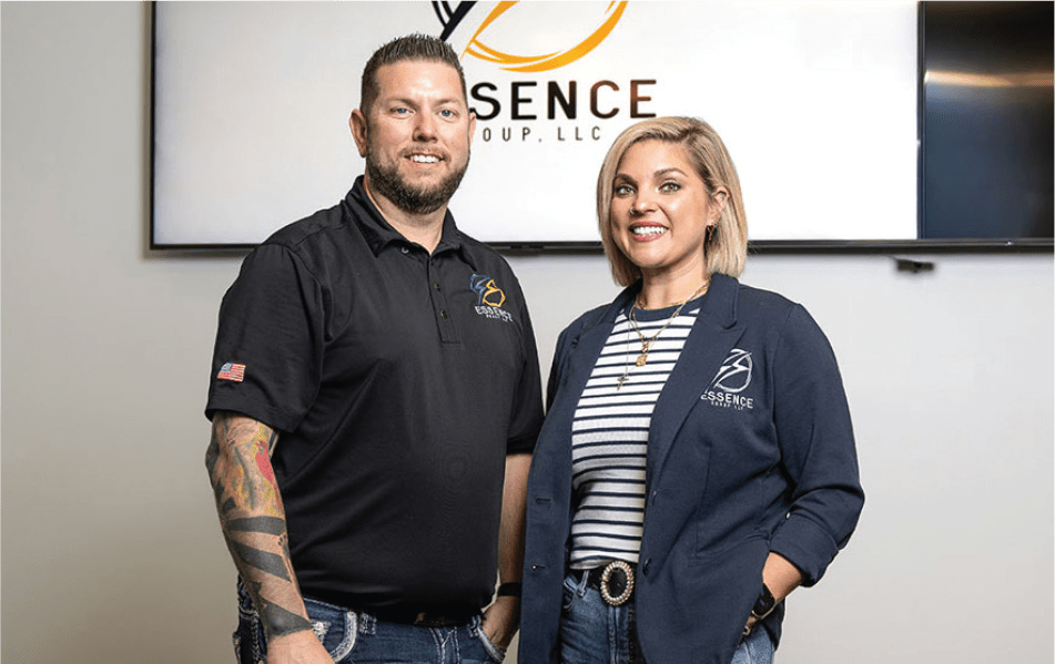 2 members of Essence Group LLC posed in front of a television set featuring their logo