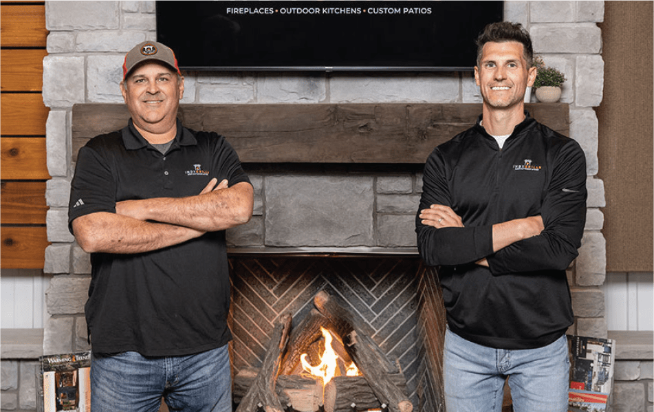 2 members of Indy Grills posed in front of a fireplace